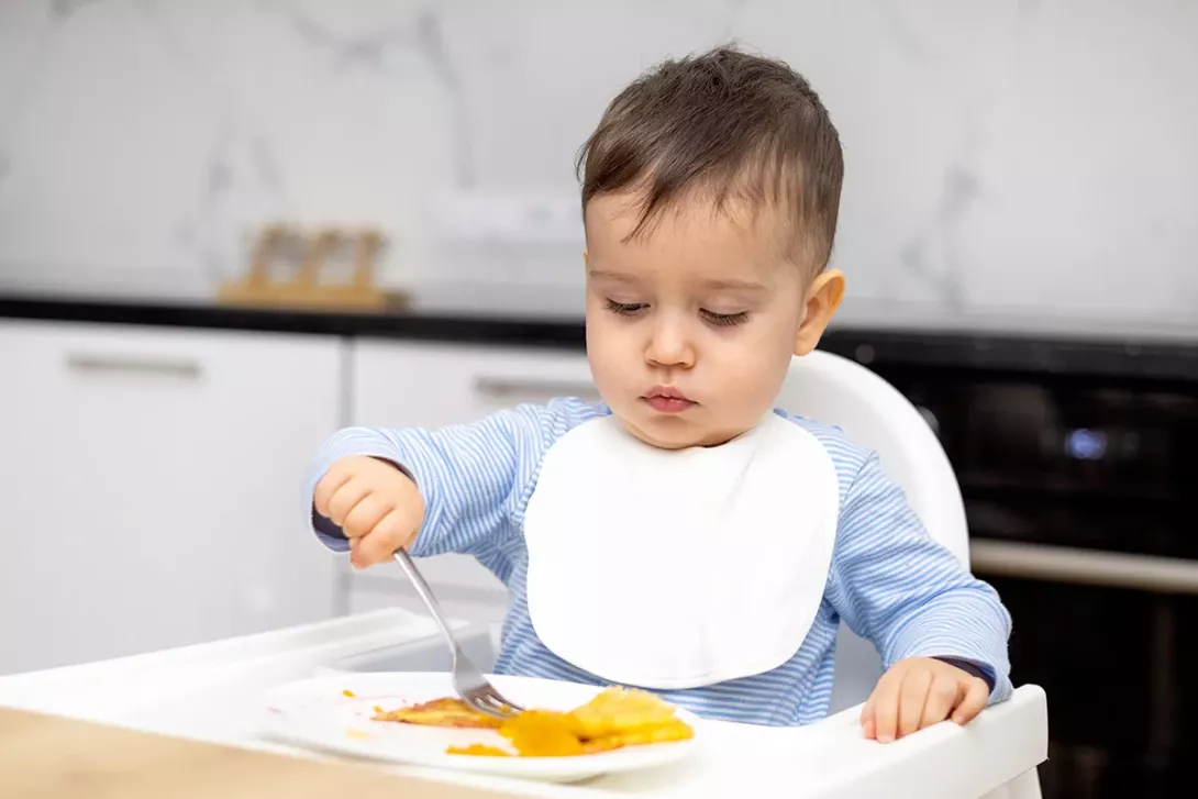 Jeune enfant mangeant seul avec une fourchette dans sa chaise haute.